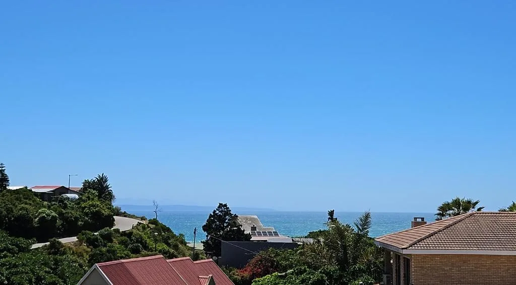 Ocean and coastline visible beyond residential rooftops and gardens