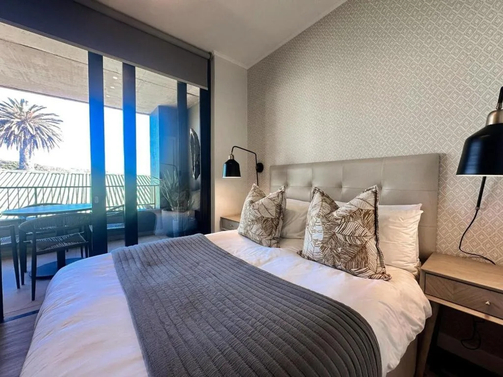 Bedroom with queen bed, ocean view through glass doors, contemporary decor