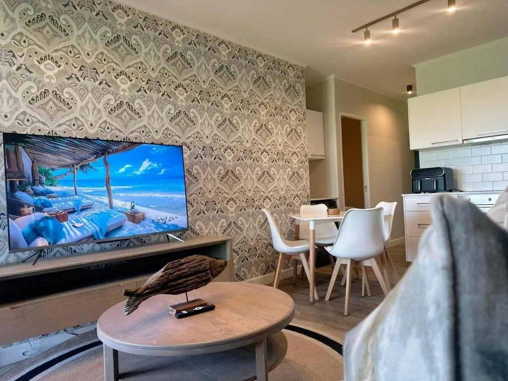 Open-plan lounge with TV, dining area, and modern kitchen visible