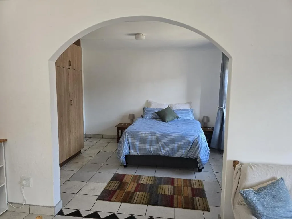 Bright bedroom with blue striped bedding and wooden wardrobe through archway