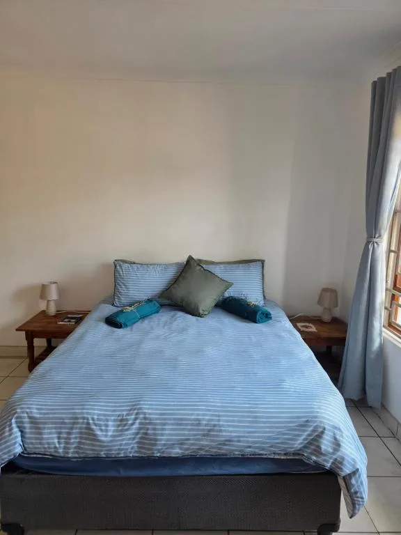 Bright bedroom with blue striped bedding, wooden side tables, and curtained window