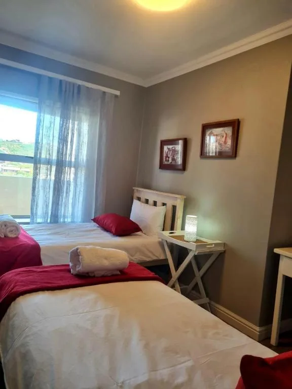 Twin bedroom with white beds, red bedding, and garden view through window