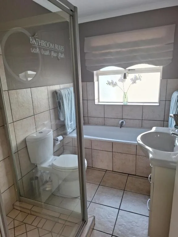 Modern bathroom with shower enclosure, bathtub, sink, and window with flowers