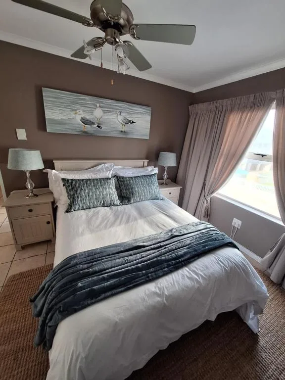Spacious bedroom with queen bed, coastal artwork, and ocean view through curtains