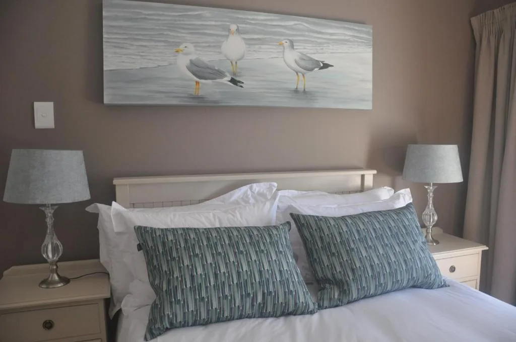 Comfortable bed with patterned pillows and seagull artwork above