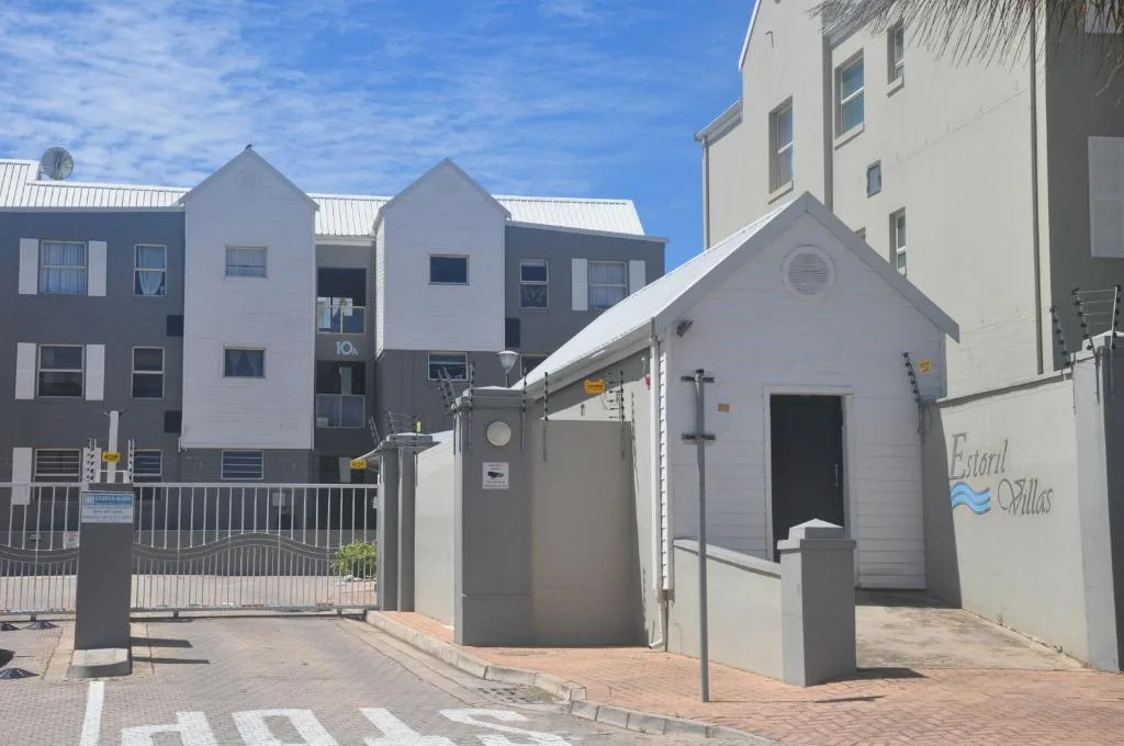Modern white apartment building entrance with gated courtyard and parking area