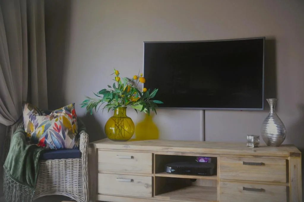 Living room with wall-mounted TV, wooden entertainment unit, and decorative flowers