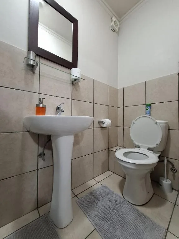 Clean bathroom with pedestal sink, toilet, and beige tile walls