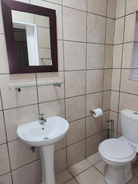 Bathroom vanity with pedestal sink, mirror, and toilet in tiled space