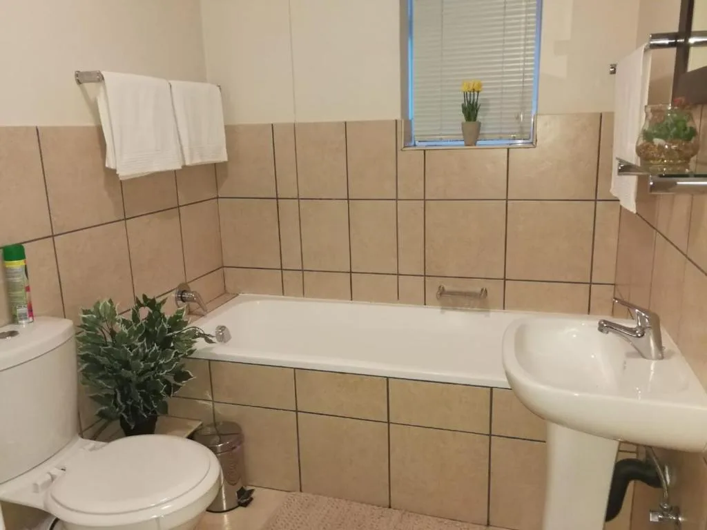 Bathroom with bathtub, pedestal sink, toilet, and beige tile walls