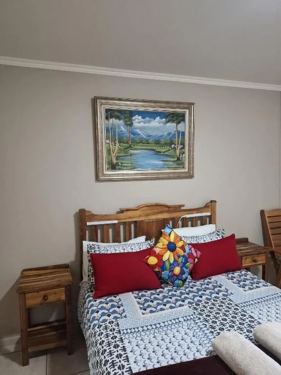 Wooden bed with patterned blue bedding and red pillows, framed landscape artwork above