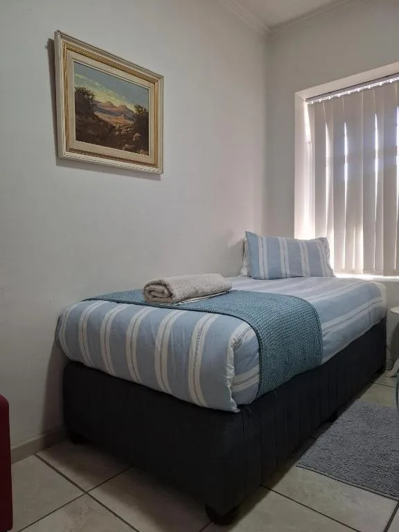 Bright bedroom with striped blue bedding, framed landscape artwork, vertical blinds
