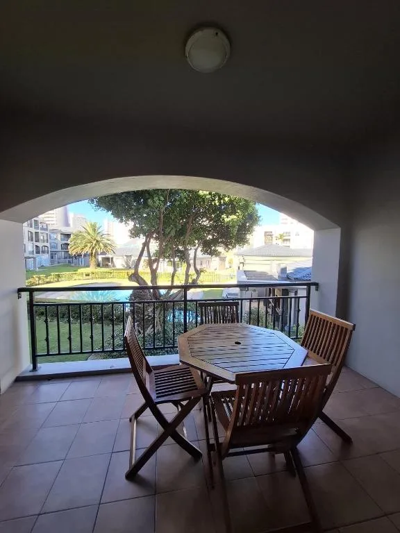 Covered balcony with dining table and chairs overlooking garden and pool area