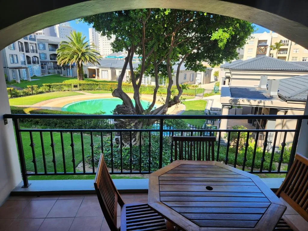 Covered balcony with wooden furniture overlooking pool and manicured gardens
