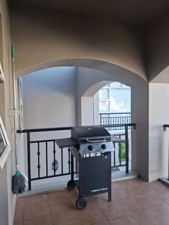 Covered outdoor deck with gas braai and black metal railing overlooking garden