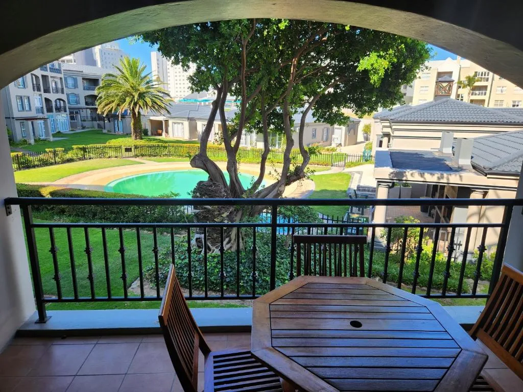 Covered balcony with wooden table overlooking lush gardens and pool