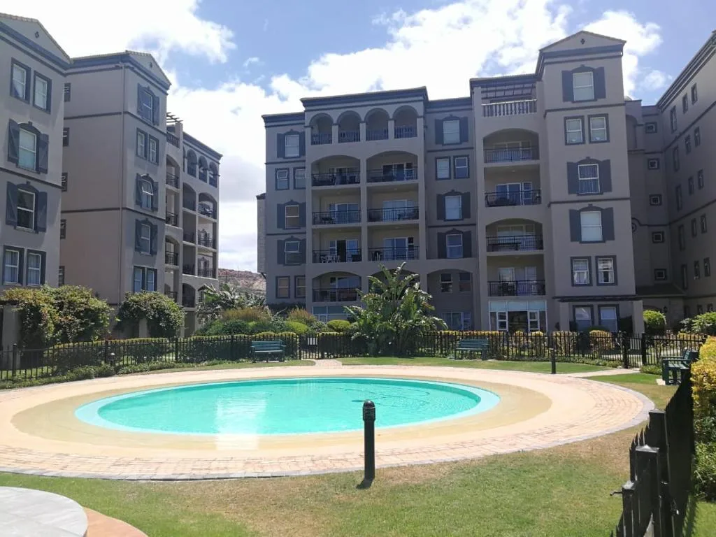 Circular swimming pool with turquoise water surrounded by manicured lawn and apartment buildings