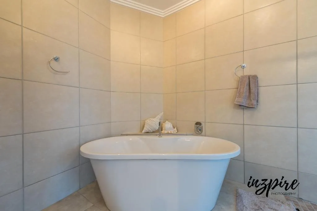 Modern freestanding bathtub in cream-tiled bathroom with towel rail