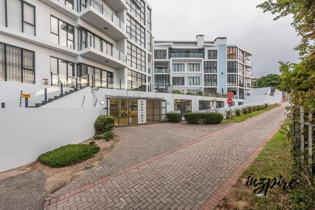 Modern multi-story apartment building with white facade and brick driveway entrance