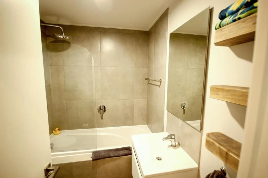 Modern bathroom with walk-in shower, white vanity sink, and wooden shelving