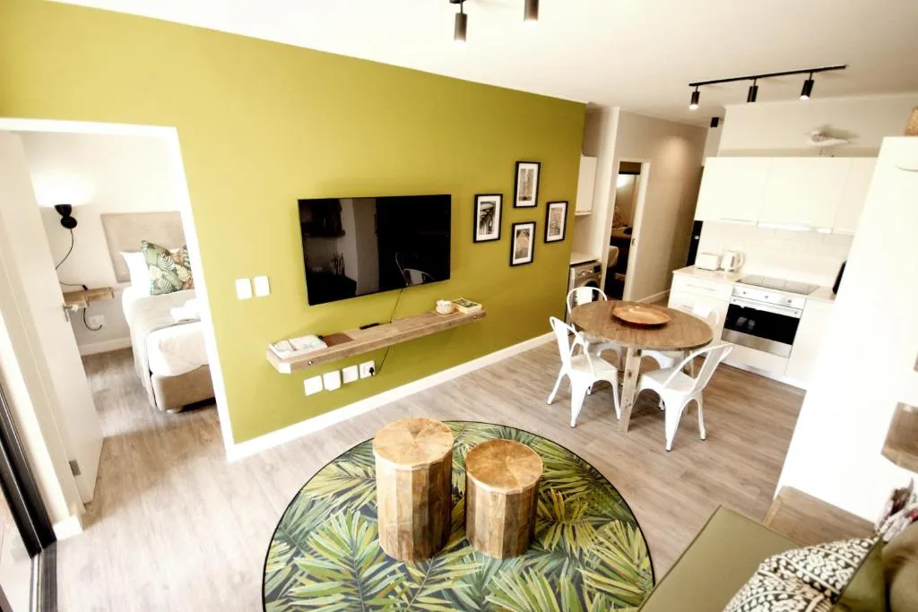 Modern lounge with bright yellow accent wall, flat-screen TV, and open-plan kitchen area
