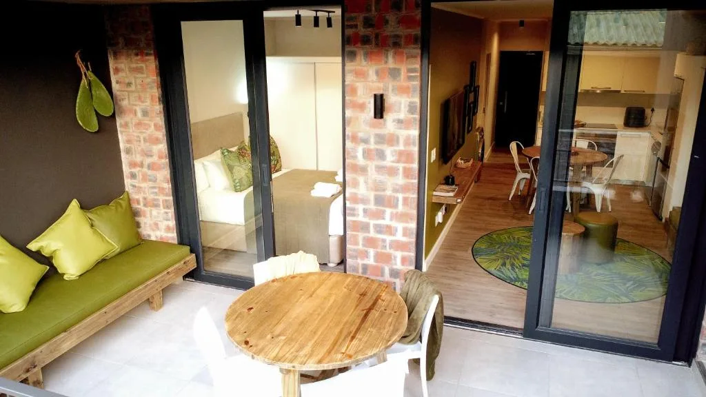 Open-plan lounge with green sofa, round wooden table, and bedroom access