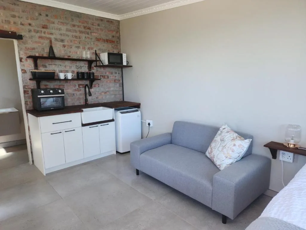 Open-plan living area with gray sofa and integrated kitchenette with brick accent wall