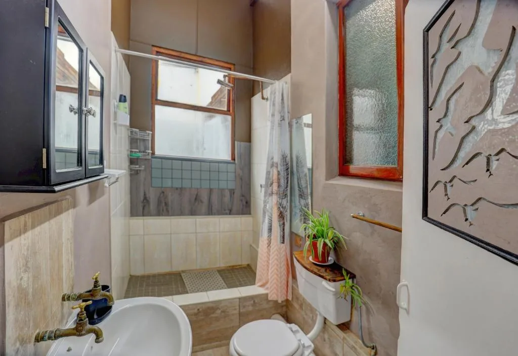 Modern bathroom with walk-in shower, white toilet, pedestal sink, and decorative wall art