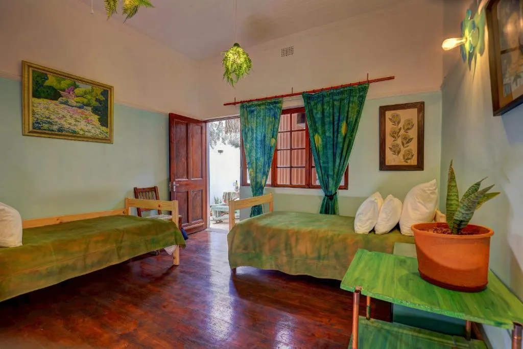 Bright bedroom with two beds, green curtains, potted plant, wooden furniture