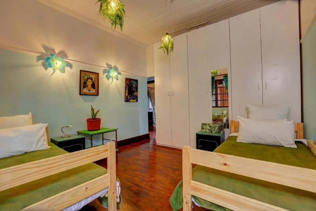 Bright bedroom with two wooden beds, green bedding, and hanging plants