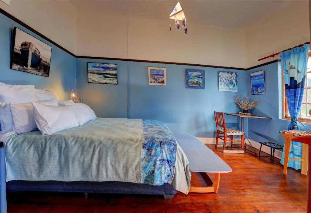 Bright blue bedroom with queen bed, ocean-themed artwork, wooden desk and chair