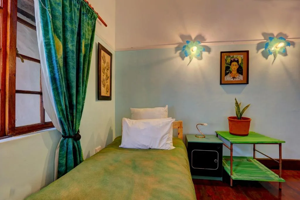 Cozy bedroom with single bed, green bedspread, colorful curtains and artwork