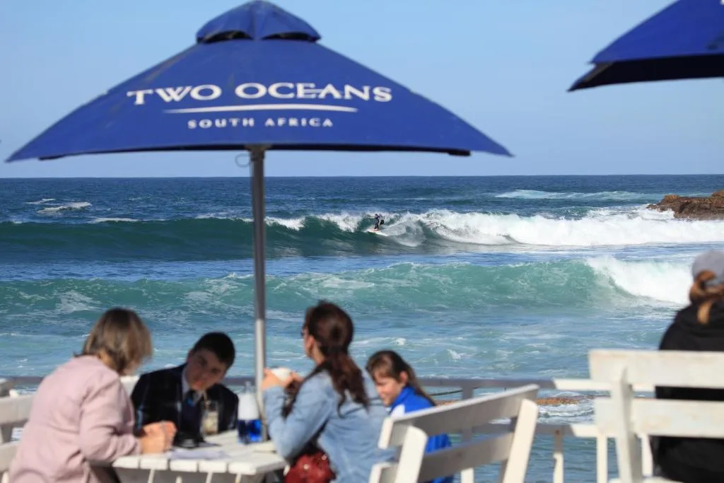 Beachfront deck with umbrellas overlooking ocean waves and surfers