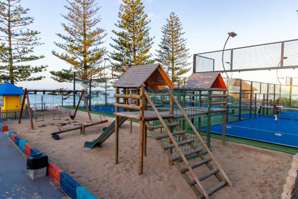 Beach playground with wooden climbing structures and tennis court facilities