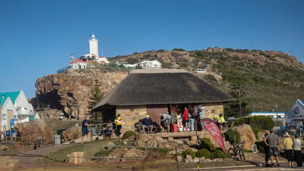 Coastal landscape with lighthouse, rocky hillside, and thatched building