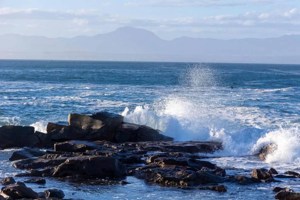 Dramatic ocean waves crashing against rocky coastline with mountains beyond