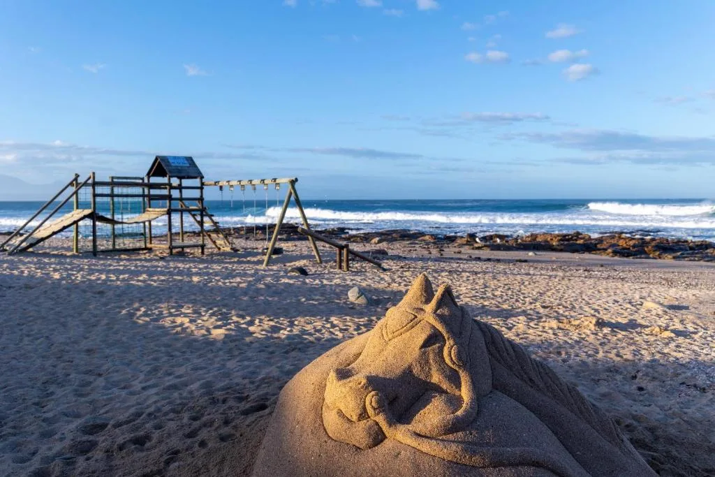 Beach with sand sculpture, playground, and ocean waves in background