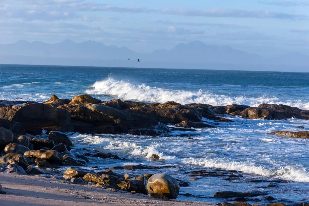 Dramatic ocean waves crashing against rocky coastline with mountains beyond