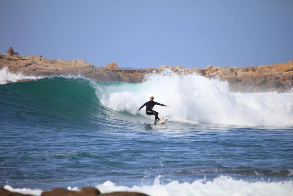 Surfer riding a wave with rocky coastline and clear blue sky