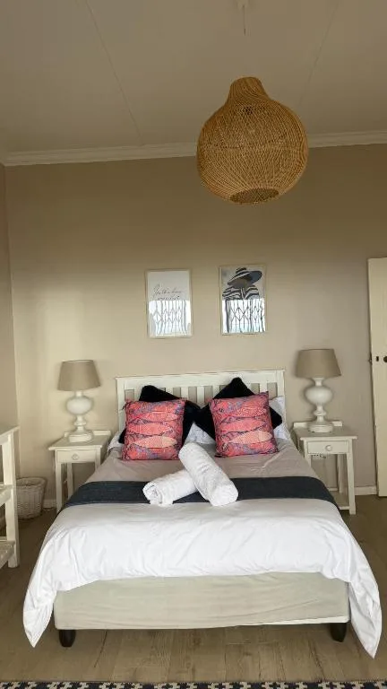 Bright bedroom with white bedding, pink patterned pillows, woven pendant light