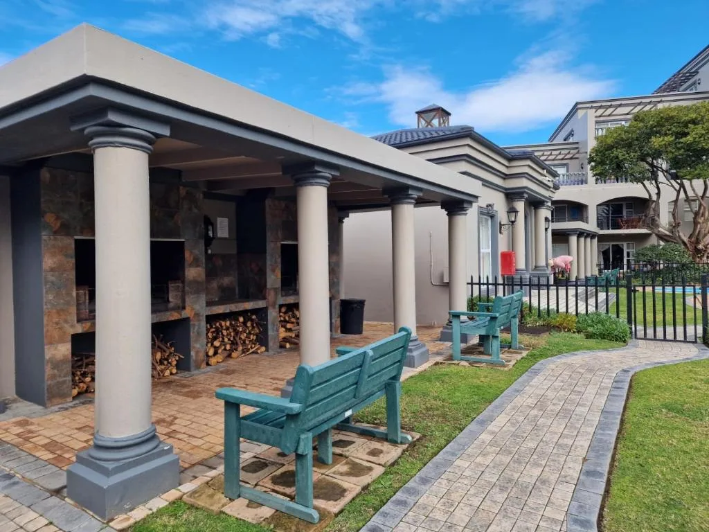 Covered braai area with columns, benches, and firewood storage outside