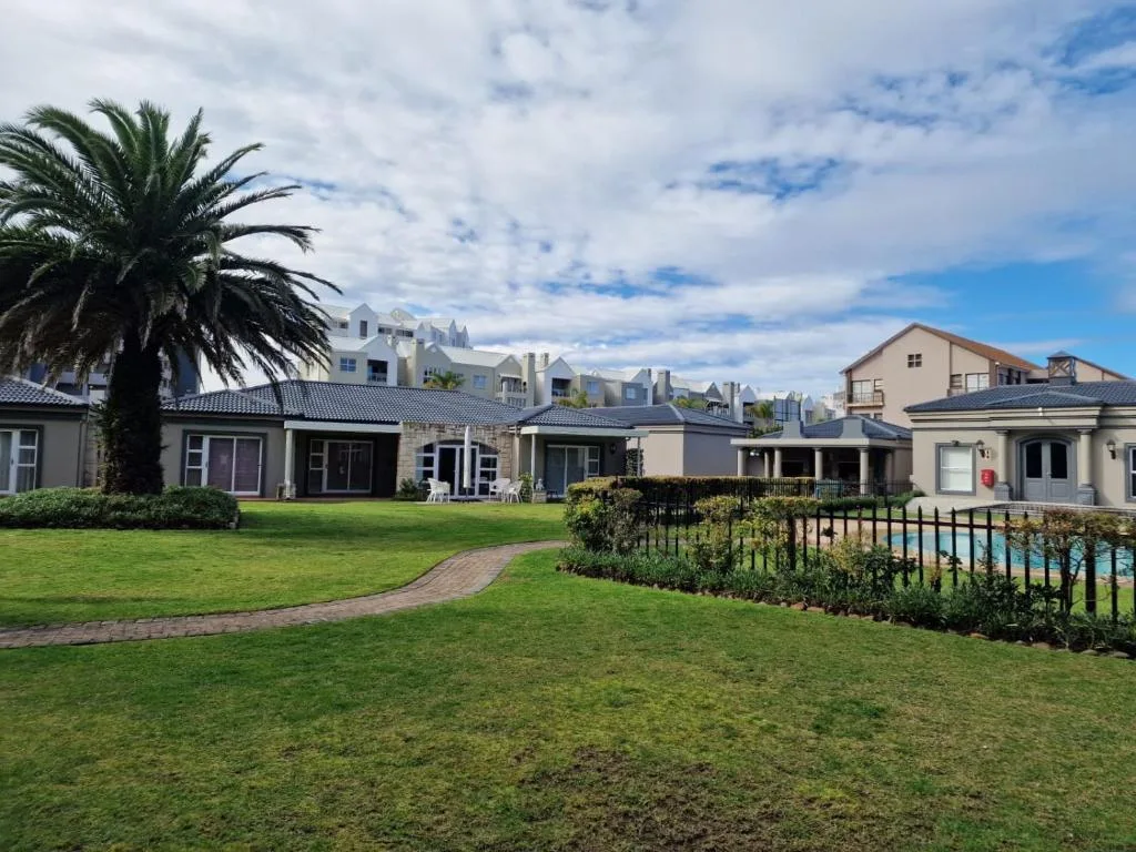 Modern apartment complex with manicured lawns, palm tree, and pool area visible