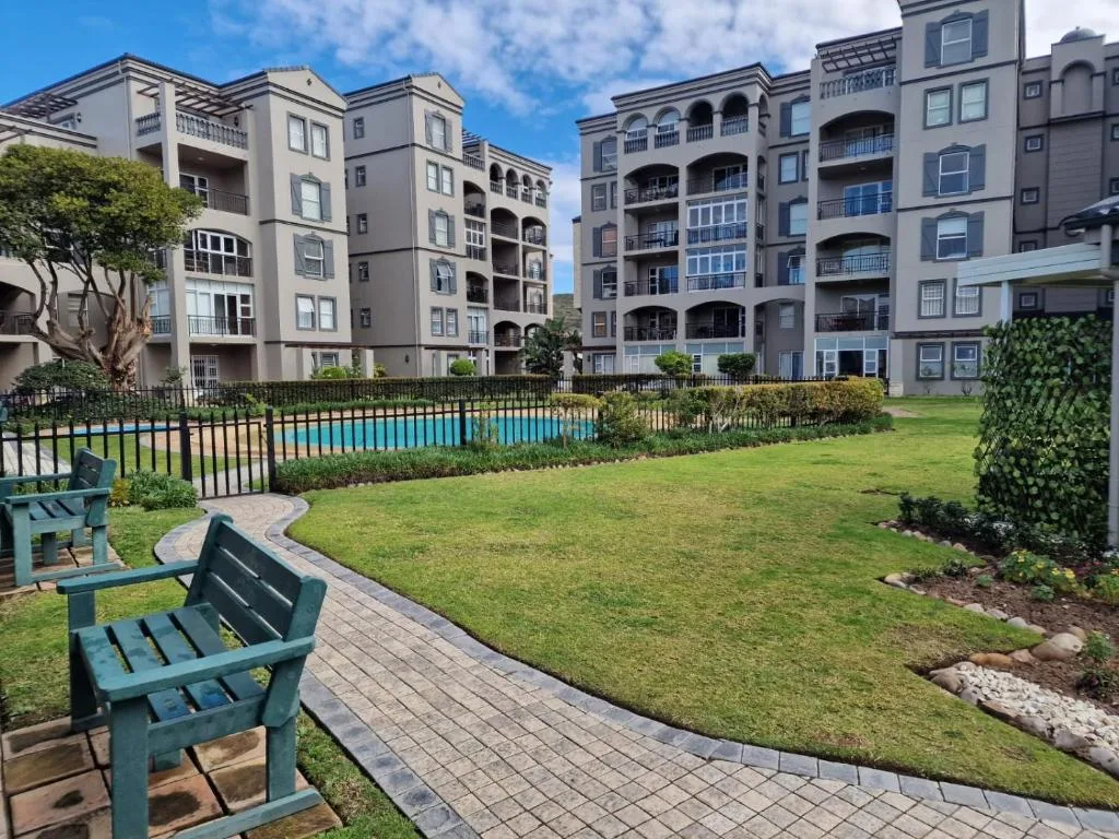 Multi-story residential building with manicured gardens, pool, and seating area