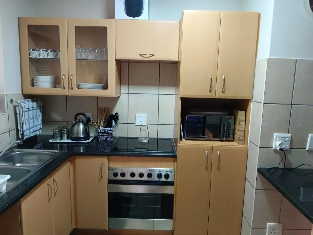 Compact kitchen with wooden cabinetry, black countertops, stove and microwave