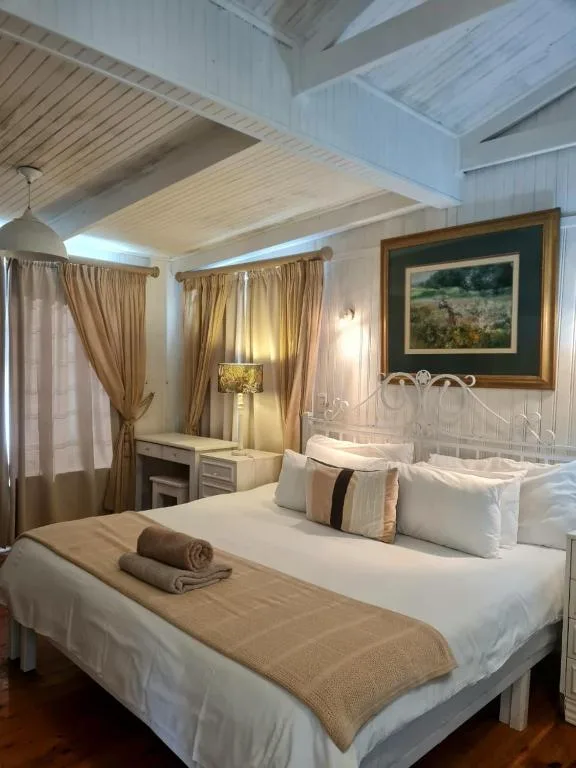 Spacious bedroom with white iron bed, cream curtains, and landscape artwork