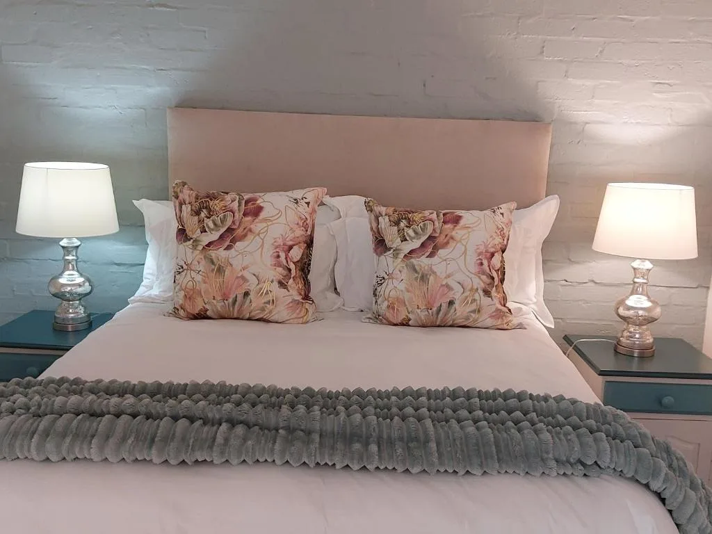 Double bed with pink headboard, floral cushions, and bedside lamps