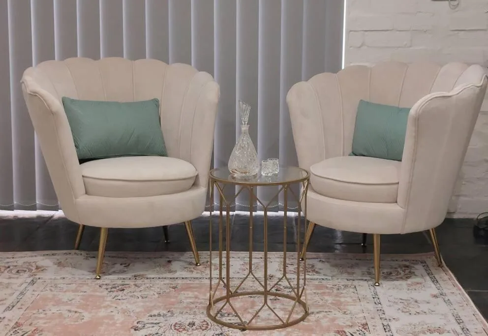 Two cream armchairs with green cushions flanking a brass side table