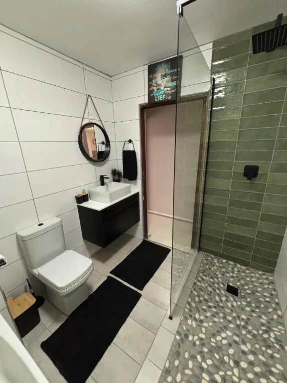 Modern bathroom with black vanity, round mirror, green tiled shower, toilet