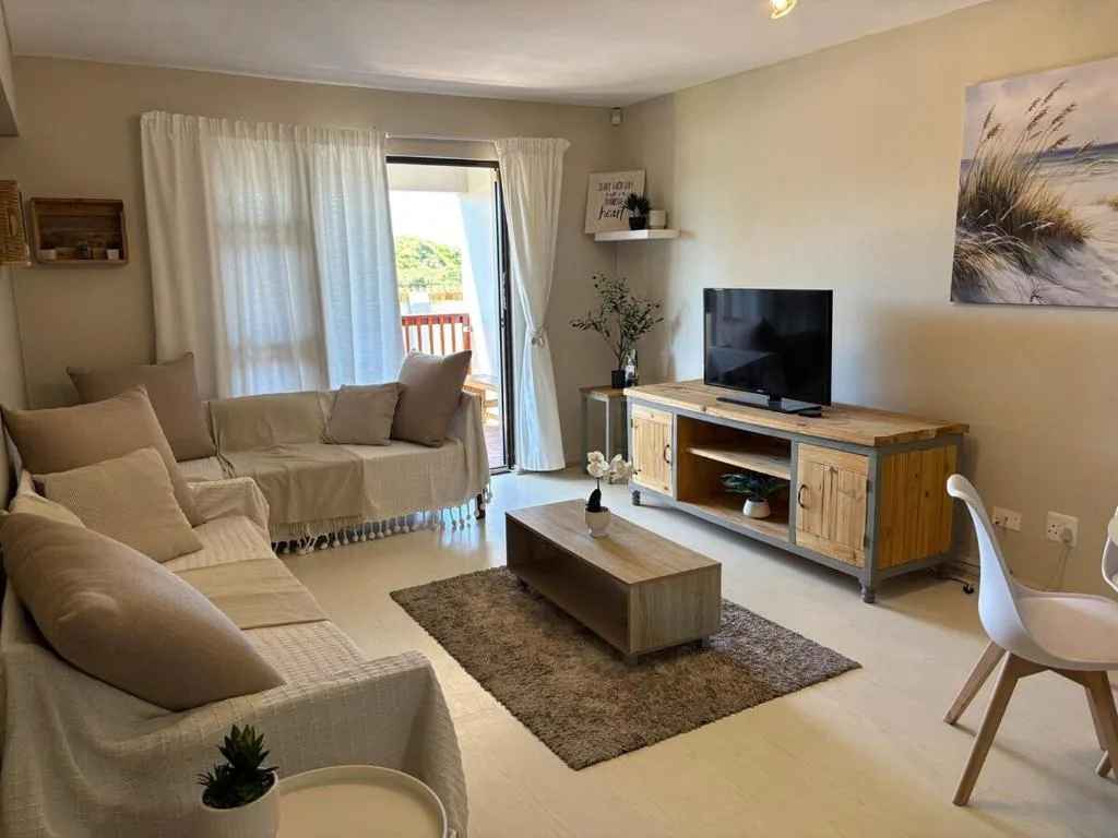 Bright lounge with cream sofas, TV unit, and glass doors opening to deck