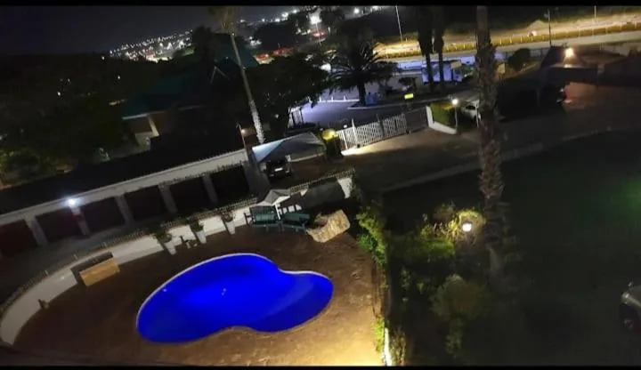 Illuminated blue swimming pool at night with property exterior and surrounding garden